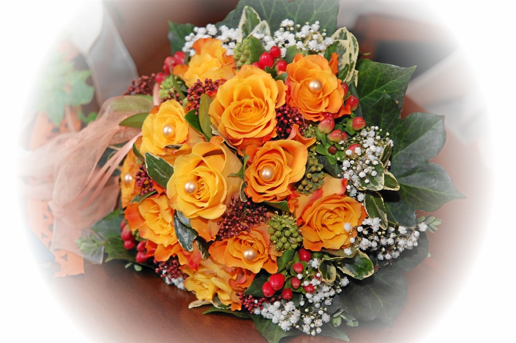 Ein üppiger Blumenstrauß mit leuchtenden orange- und gelben Rosen, kombiniert mit weißen Füllblumen und roten Beeren.